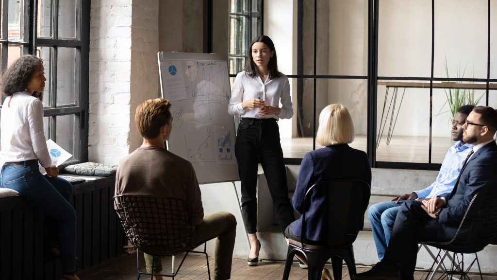 Young white female, standing infront of a white board, leading a team training session